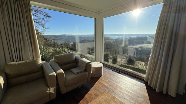 A spacious room with a large window offering a view of the countryside. There is a beige sofa and a wooden floor. - Panoramic Villa With Private Sauna in Erezee (Erezee)