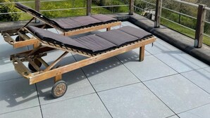 A wooden deck with two sun loungers, a metal railing, and a view of rolling hills. - Panoramic Villa With Private Sauna in Erezee (Erezee)