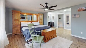 Une chambre à coucher avec un lit, une commode en bois, une chaise et un ventilateur de plafond.
