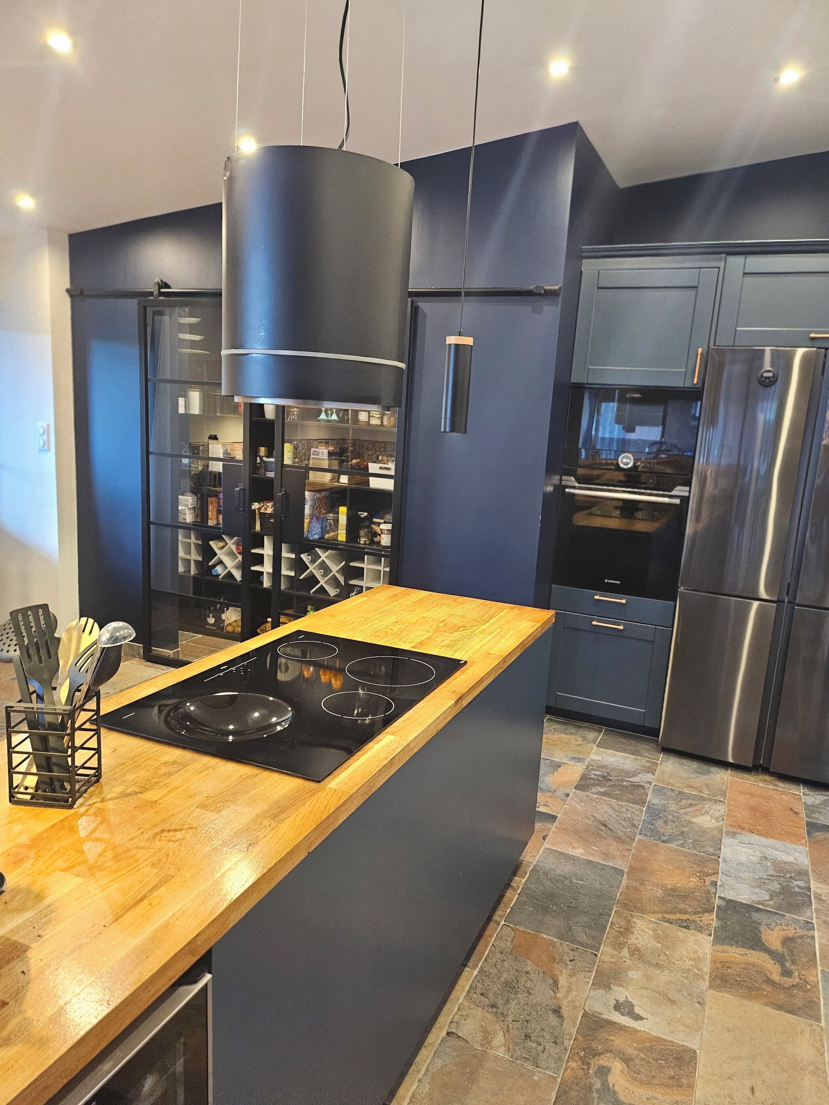 Una cocina moderna con una isla central, electrodomésticos integrados y piso de baldosas de piedra.