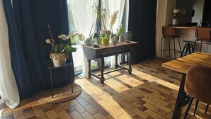 A room with a wooden table, chairs, a potted plant, and a view through a window with curtains.