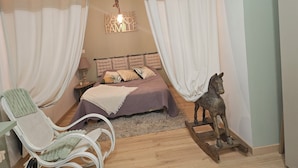 A bedroom with a bed, a chair, a nightstand, a lamp, a decorative horse statue, and a hanging light fixture.