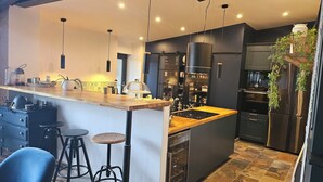 A modern kitchen with a wooden island, bar stools, stainless steel appliances, and a hanging plant.