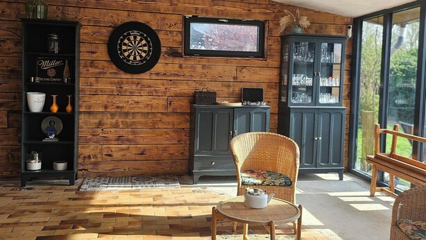A cozy room with a wooden wall, a dartboard, a television, and wicker furniture.