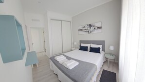 Moderni hotellihuone, jossa on suuri sänky, yöpöydät, peili ja taulu seinällä.