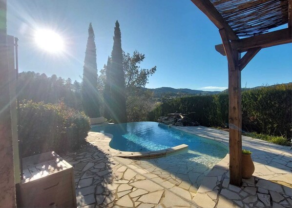 Relax by the serene pool surrounded by lush greenery and a wooden pergola.