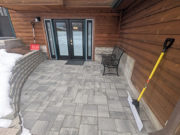 A covered patio area with stone flooring, a bench, a broom, and a door with glass panels.