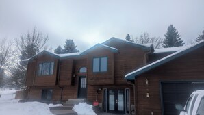 Una casa de madera de dos pisos con un garaje, rodeada de nieve.