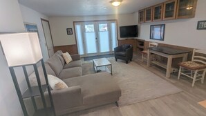 Una sala de estar con sofá, mesa de centro, televisor, aparador de madera y un comedor con mesa y sillas.