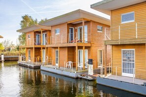 A row of wooden cabins with balconies, connected by a dock, situated by a calm body of water. - Hausboot in Barth am Barther Bodden (Barth)