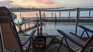 A wooden dock with chairs and a table, a box labeled 'Beker,' and a view of a calm body of water with a dock in the background. - Hausboot in Barth am Barther Bodden (Barth)