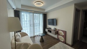 Une chambre d’hôtel moderne équipée d’un canapé, d’une table à manger, d’un téléviseur et d’une grande fenêtre avec des rideaux.