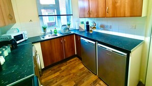 Una cocina con armarios de madera, encimera negra, lavavajillas y una ventana con persianas.