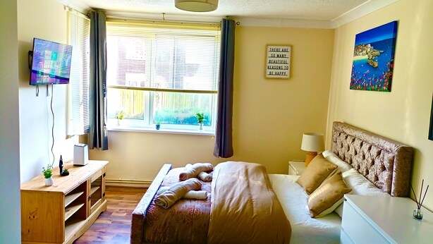 Un dormitorio con cama, mesita de noche, lámpara, televisor y ventana con cortinas.