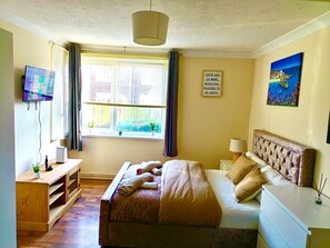 A bedroom with a bed, bedside table, lamp, TV, and a window with curtains. - Stylish 2-bed home in Telford (Telford)