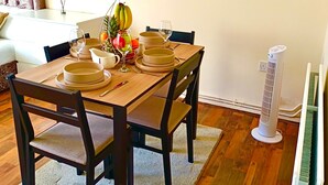 Un comedor con una mesa de madera dispuesta para cuatro personas, rodeada de sillas oscuras. Hay elementos decorativos en las paredes, incluyendo pequeñas macetas y un cuadro enmarcado.