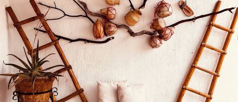 Une pièce rustique décorée d’une œuvre d’art murale faite de branches tressées, d’une échelle en bois, d’un banc et d’une plante en pot.