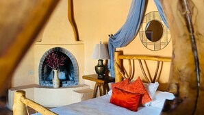 Ein gemütliches Zimmer mit Bett, einem kleinen Tisch mit Lampe, einem Kamin und einem Fenster mit Vorhängen.