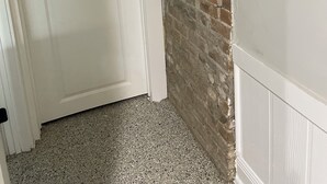 Un pasillo con una puerta blanca, un muro de ladrillo y un revestimiento blanco en la pared.