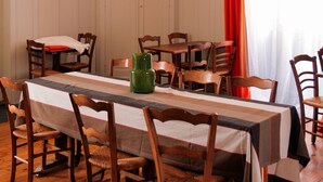 Zona pranzo con un tavolo lungo, diverse sedie, lampadari sospesi e una tenda rossa.