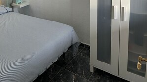 Ein Schlafzimmer mit Bett, Schrank, Deckenventilator und einer kleinen Ablagefläche mit einer Vase.