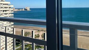 Ein Balkon mit Blick auf den Ozean, einen Strand und eine ferne Stadtansicht.