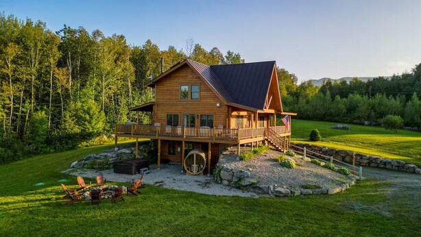 A wooden cabin with a deck, surrounded by a well-maintained lawn and trees. - Luxury Lodge in NH: Ski, Hottub, Sauna, Pool Table, Playscape, Game Room & Hike (Jefferson)