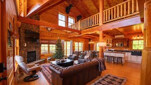 A spacious log cabin with a stone fireplace, a dining area, and a kitchen. - Luxury Lodge in NH: Ski, Hottub, Sauna, Pool Table, Playscape, Game Room & Hike (Jefferson)