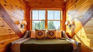 A cozy log cabin room with a bed, two wall-mounted lamps, and a large window. - Luxury Lodge in NH: Ski, Hottub, Sauna, Pool Table, Playscape, Game Room & Hike (Jefferson)