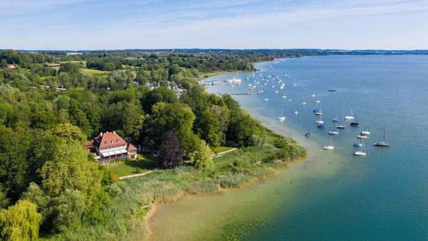 An aerial view of a coastal area with a house surrounded by lush greenery and a marina with several boats. - Cozy Bavarian home with fireplace and fully equipped kitchen. (Moorenweis)