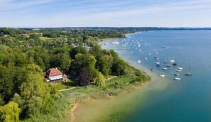 Une vue aérienne d’une zone côtière, avec une maison entourée d’une végétation luxuriante et une marina où sont amarrés plusieurs bateaux.