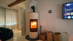 A modern living room with a wood-burning stove, a TV mounted on the wall, and a cozy seating area. - Cozy Bavarian home with fireplace and fully equipped kitchen. (Moorenweis)