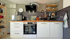 A modern kitchen with white cabinetry, a built-in oven, a microwave, and a clock on the wall. - Cozy Bavarian home with fireplace and fully equipped kitchen. (Moorenweis)
