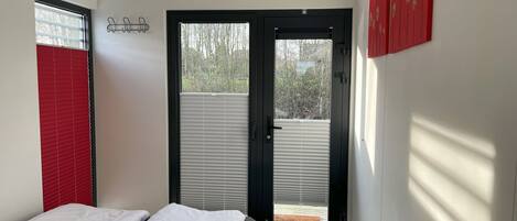 A bedroom with a bed, a door leading to a balcony, and a red decoration on the wall.