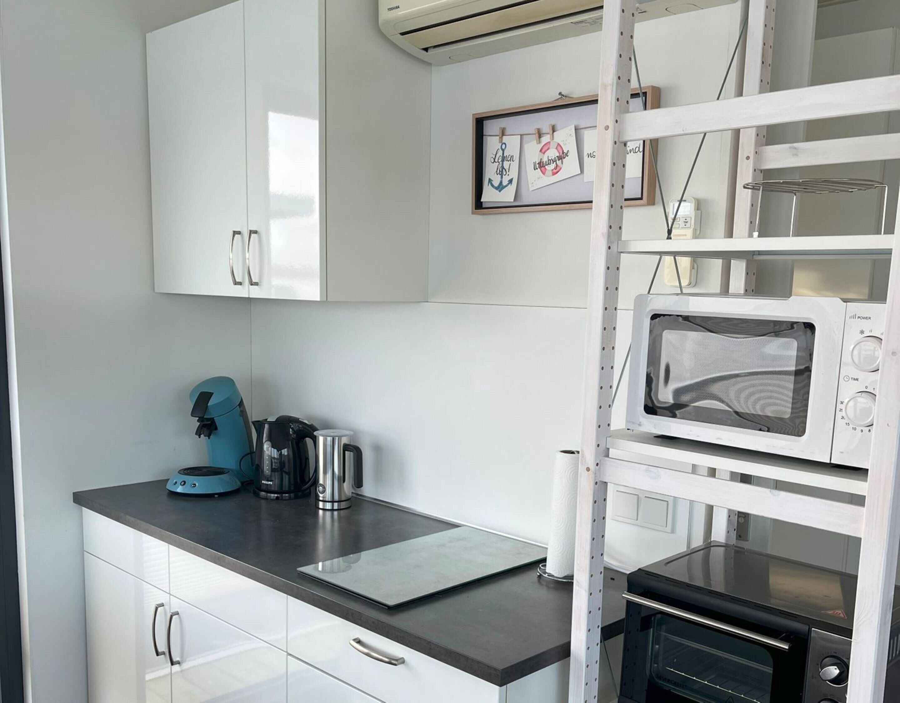 A compact kitchen with white cabinets, a microwave, a toaster oven, and a kettle on the counter.