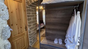 Een rustieke kamer met een houten deur, stenen muren, een stapelbed met wit beddengoed en een kroonluchter.
