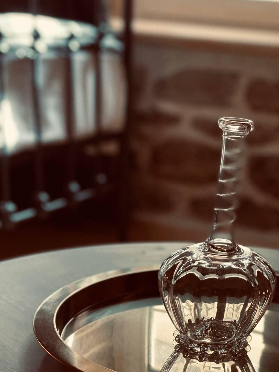 Une bouteille en verre transparent, à col étroit et à base arrondie, posée sur une surface réfléchissante.