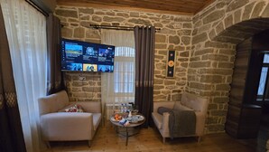 Een gezellige woonkamer met stenen muren, twee banken, een salontafel en een televisie waarop een muziekzender draait.