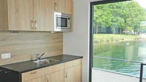 Eine moderne Küche mit Holzausstattung, einer Edelstahl-Mikrowelle und einem großen Fenster mit Blick auf einen See.
