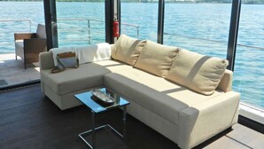 Ein moderner Außenbereich mit einer Sitzecke, einer Couch, Stühlen und einem kleinen Tisch, mit Blick auf das Wasser.