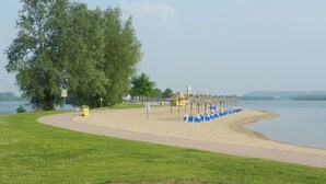 Ein Park am Seeufer mit Sandstrand, einer Reihe blauer Stühle und einem großen Baum.