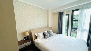 Habitación de hotel con una cama grande, una mesita de noche, una lámpara y vistas a zonas verdes por la ventana.