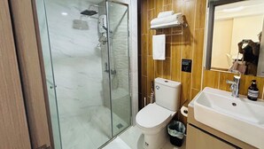 Un baño moderno con ducha envuelta en vidrio, inodoro y lavamanos con espejo.
