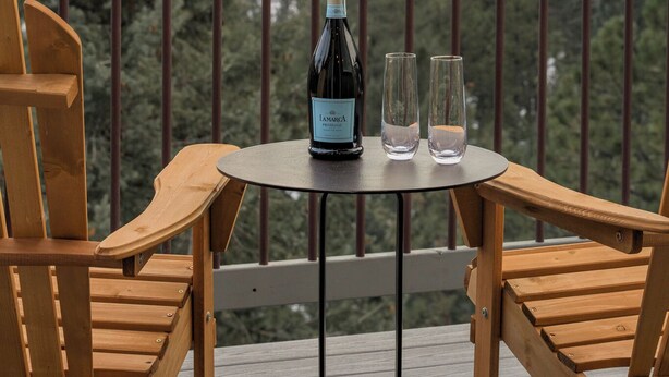 Un pontile in legno con due sedie e un tavolo, una bottiglia di vino e due bicchieri sul tavolo.