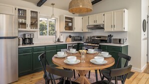Una cucina moderna con mobili bianchi, un tavolo rotondo in legno e un lampadario in vimini.