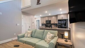Ein Wohnzimmer mit einem grünen Sofa, einem Couchtisch und einem an der Wand befestigten Fernseher.