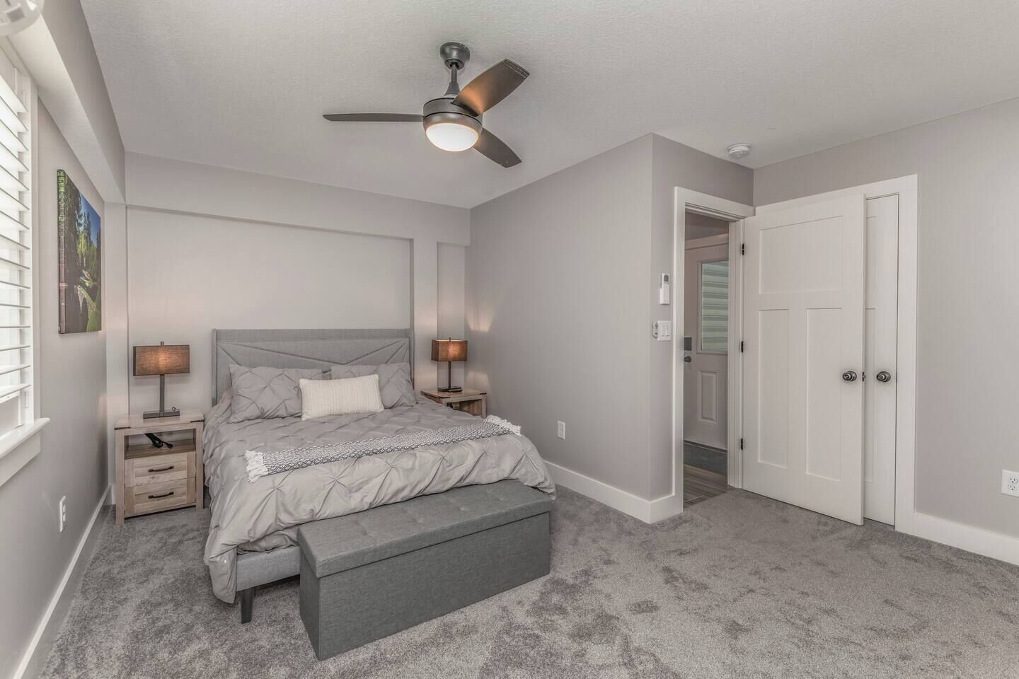 Un dormitorio con cama, mesitas de noche, un banco, un ventilador de techo y una puerta.