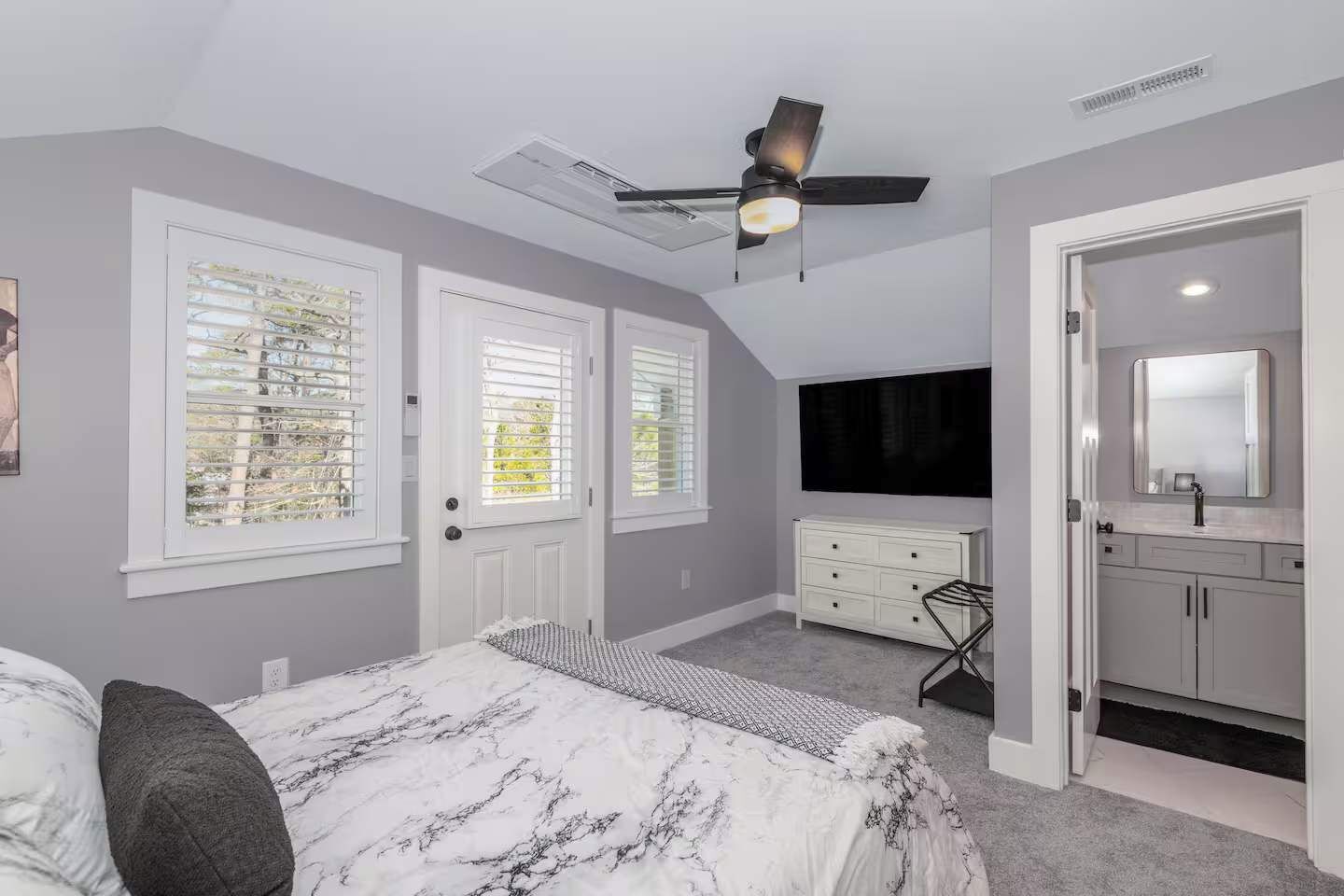 A bedroom with a bed, a dresser, a vanity with a mirror, and a ceiling fan.