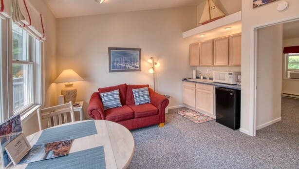 A compact living space with a kitchenette, a red sofa with striped pillows, a dining table with a placemat, and a framed picture on the wall. - DePerrys On The Lake Waterfront Access to Lake Superior (Bayfield)