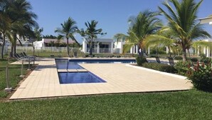 A swimming pool with a tiled deck, surrounded by palm trees and a fence.